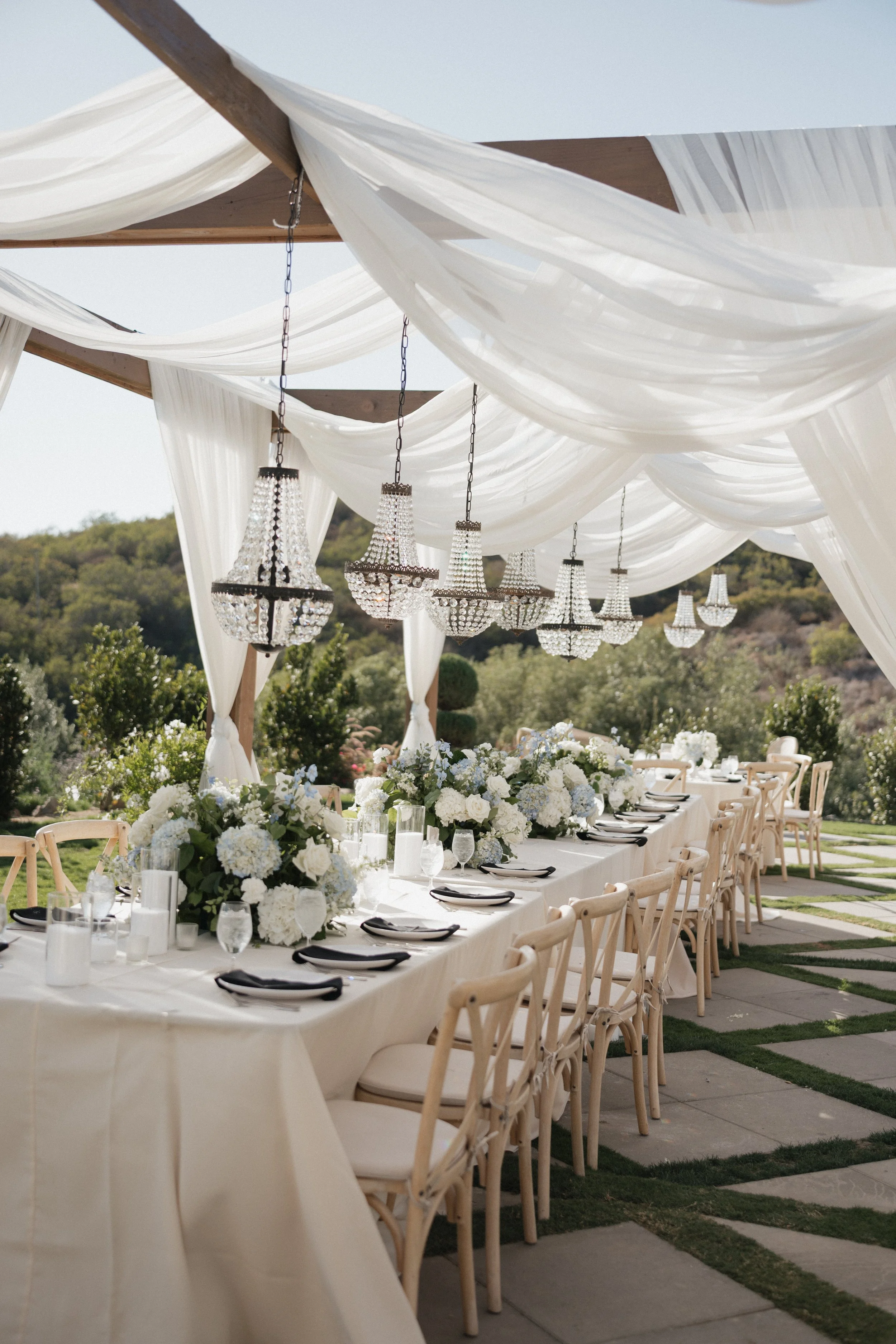 Wedding reception table details with hydrangeas, place settings, table, chandeliers at Jeune Perché in Oceanside, California by Jennifer Noelle