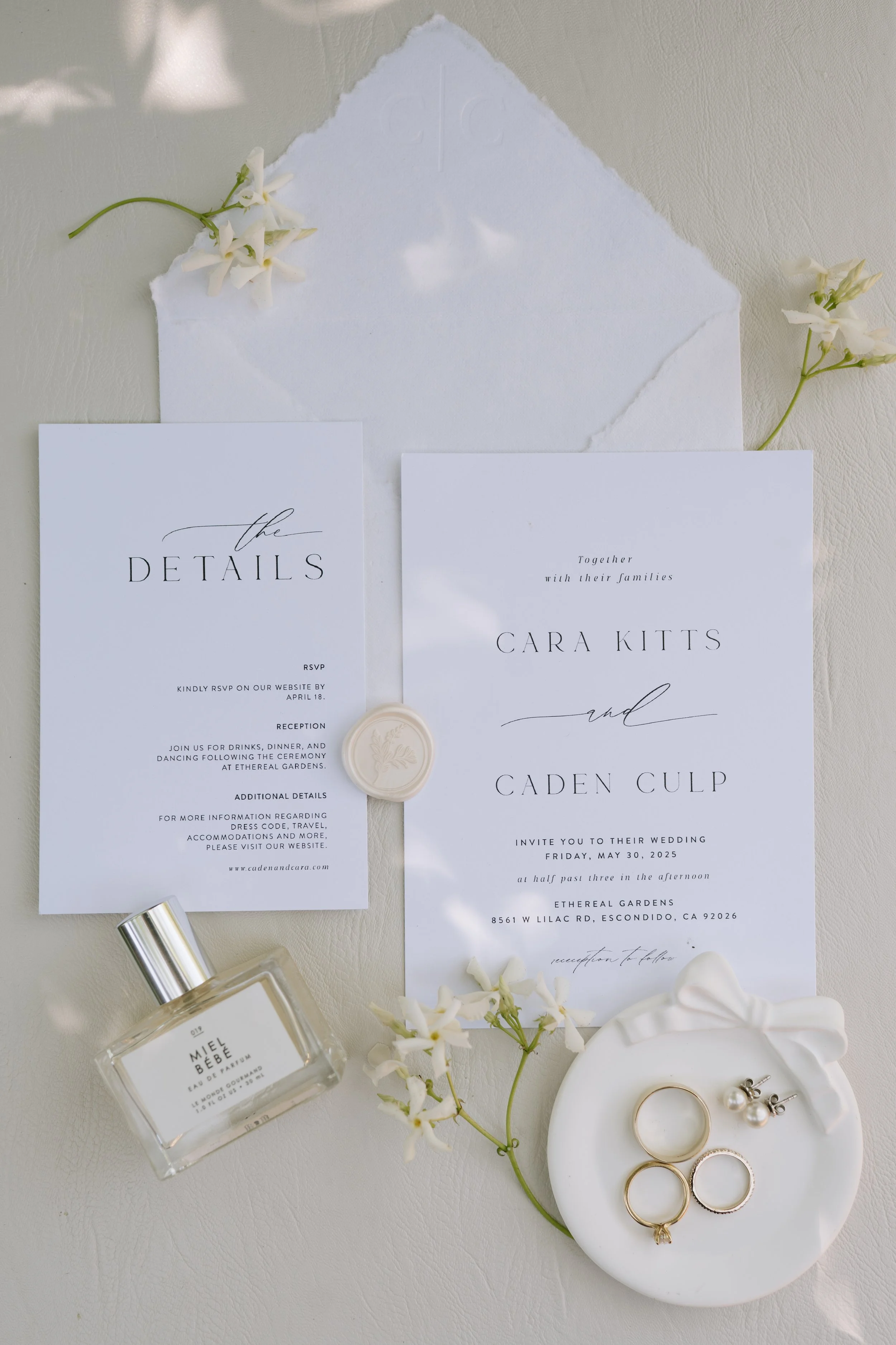 Wedding detail featuring invitation suite, florals, rings, and perfume at Ethereal Gardens