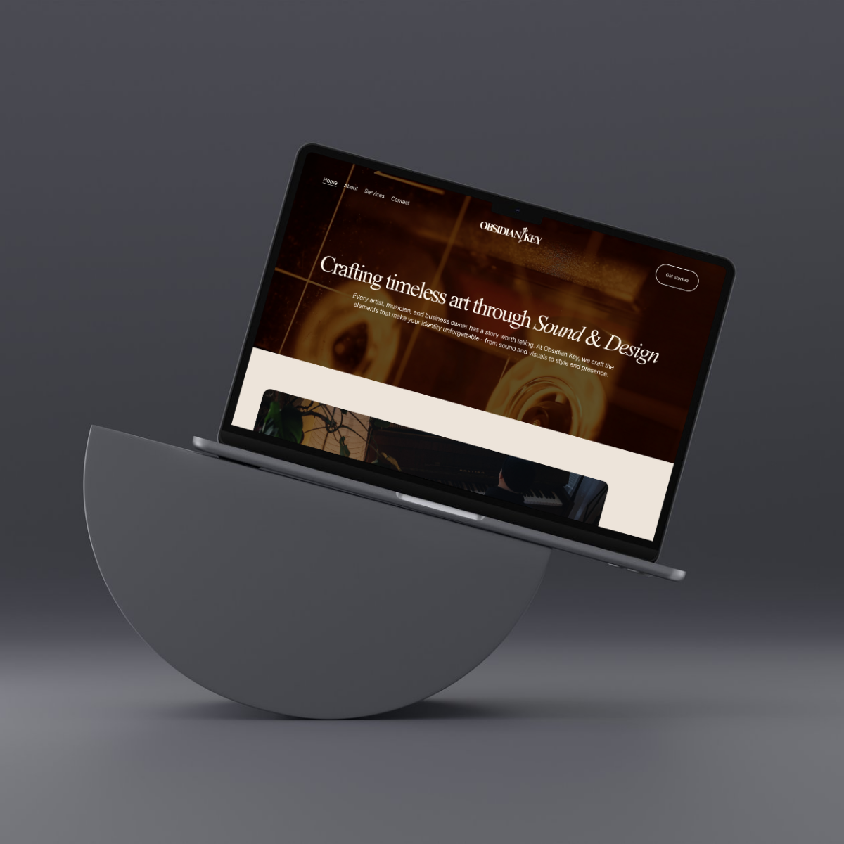 A tablet displaying the homepage of the Obsidian Key website, which features a dark brown background image and white text that reads "Crafting timeless art through Sound & Design." The tablet is positioned at an angle and is balanced on a semi-circular gray stand against a dark gray background.