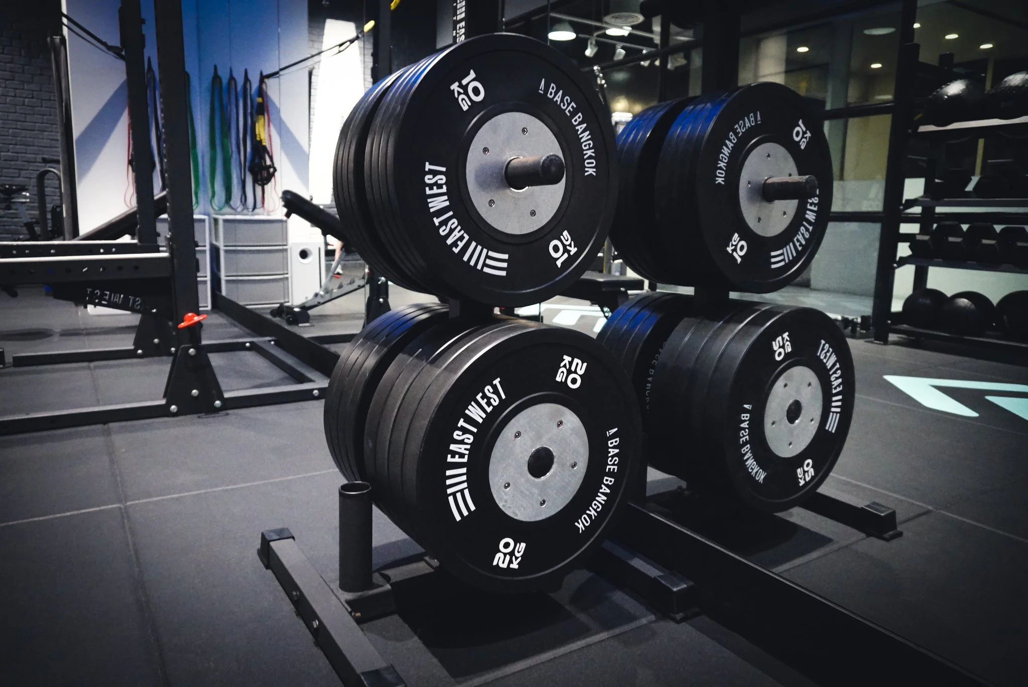 A rack of weight plates on a fitness gym floor. The plates are black with white lettering, stacked and ready for use.