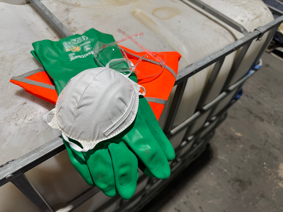 Personal protective equipment on a metal cart, including green gloves, safety glasses, a face mask, and a reflective orange safety vest.