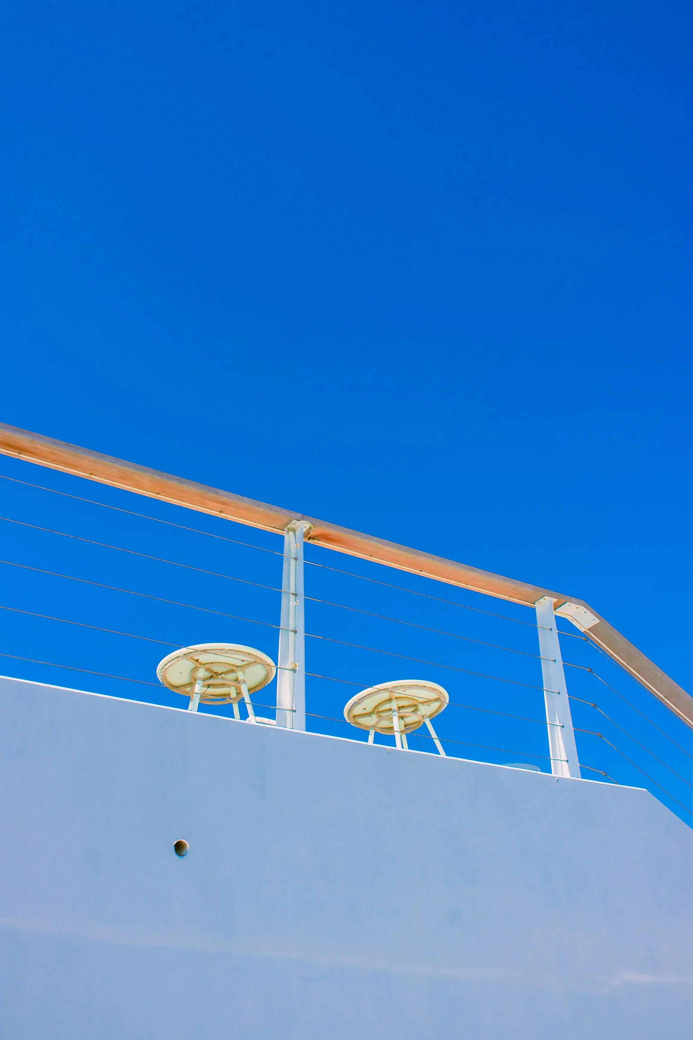 A clear blue sky behind a modern balcony with two circular chairs and a wooden handrail.