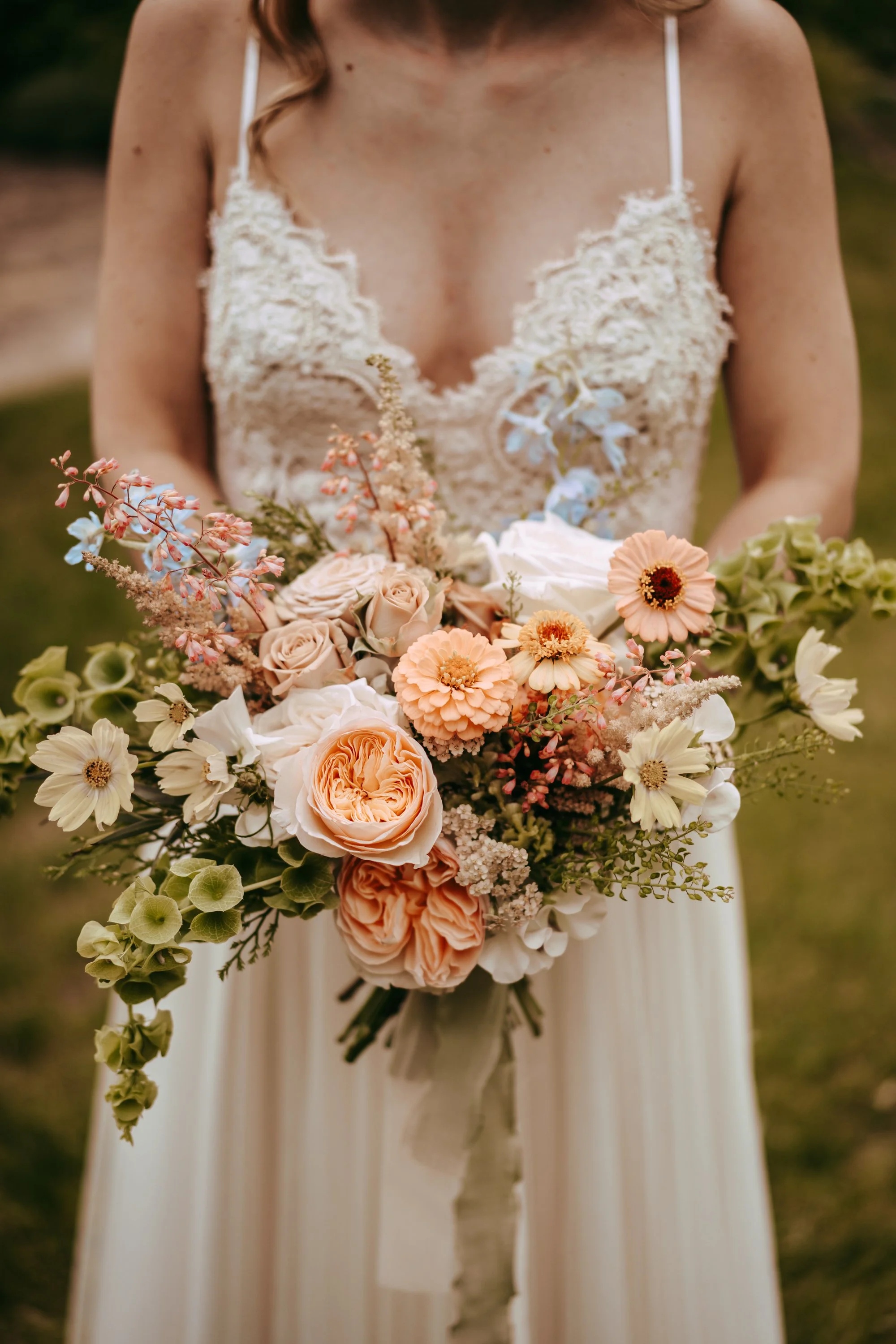 Bride holding a bouquet of assorted flowers including roses, daisies, and greenery, outdoors.