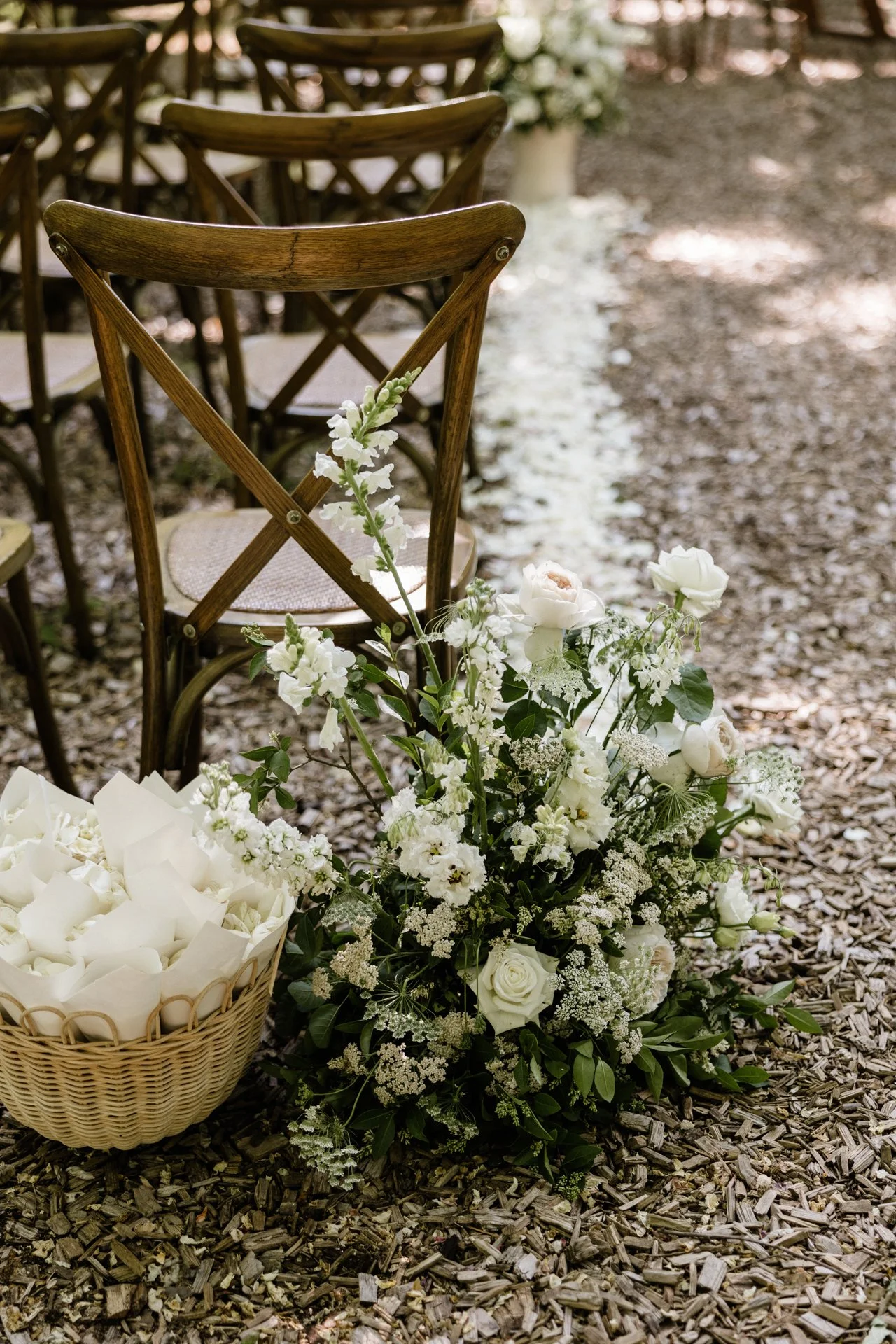 Wedding or event decoration with white flowers and chairs on bark mulch ground.
