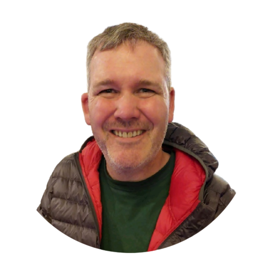 Smiling man with short gray hair, wearing a dark puffer jacket with red lining, and a green shirt, against a white background.