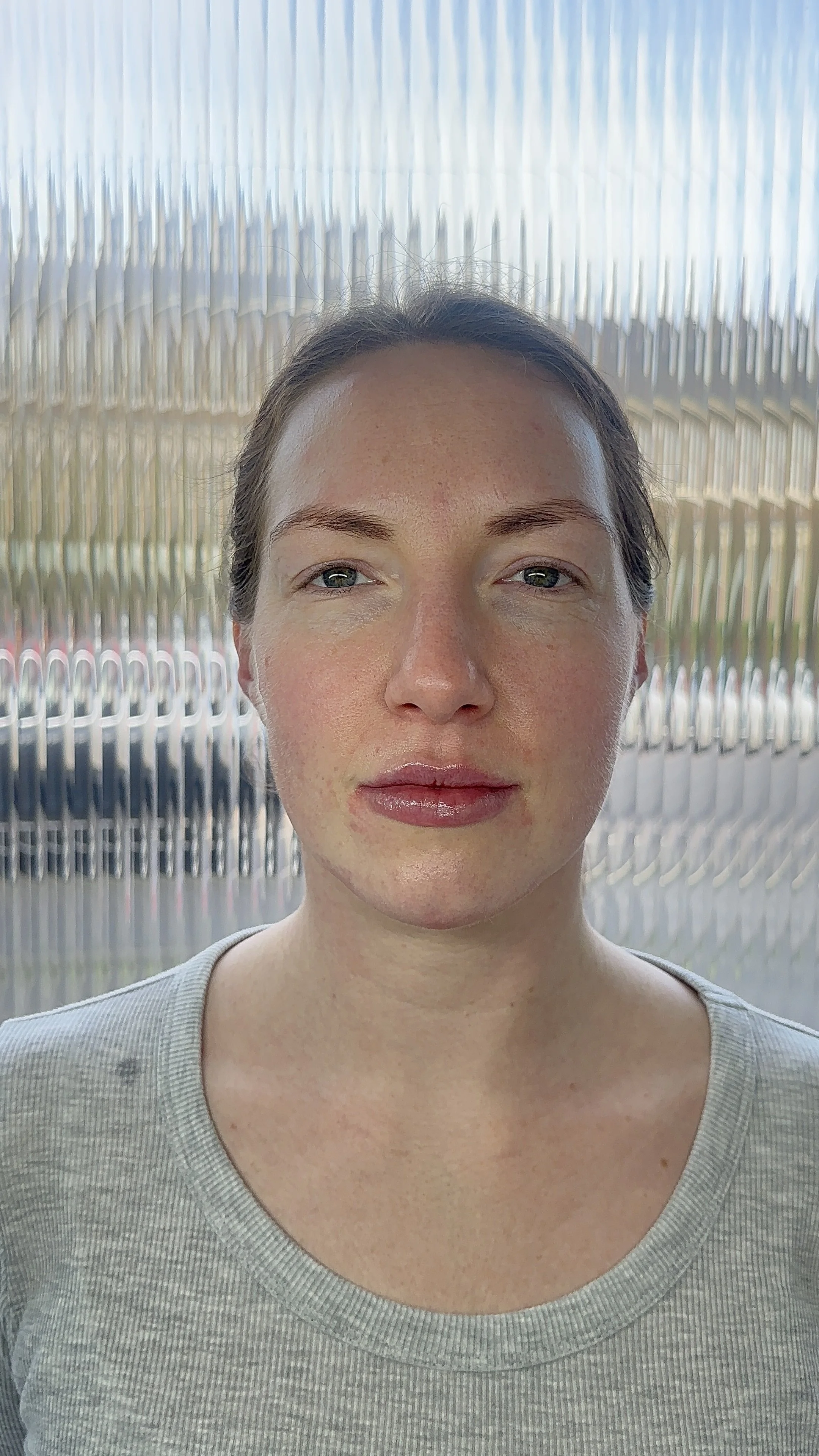 Close-up of a woman with light skin, brown hair, and blue eyes standing in front of a textured background.