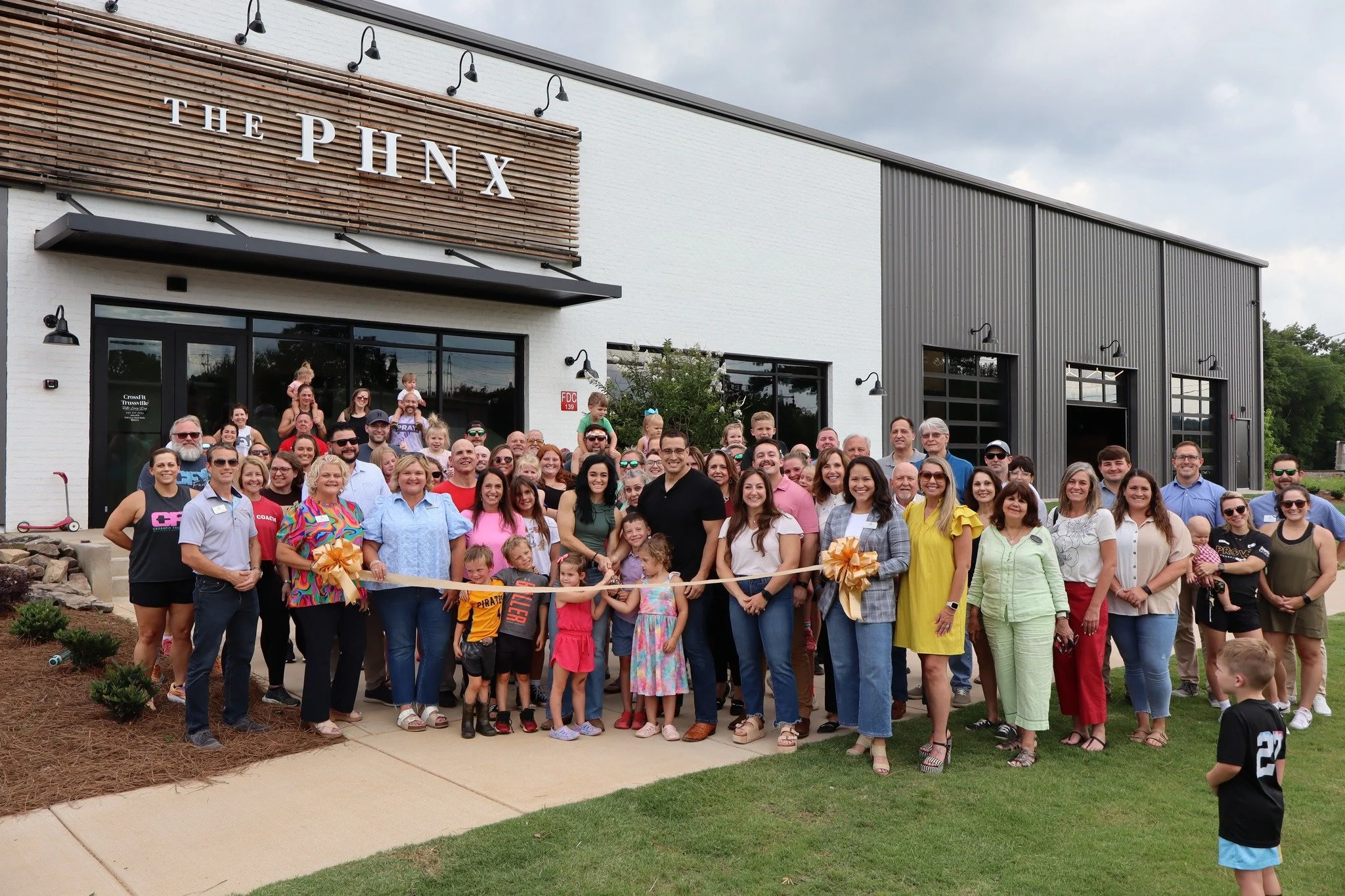 Group of people gathered for a ribbon cutting ceremony in front of a modern building with the sign 'The Phx'.