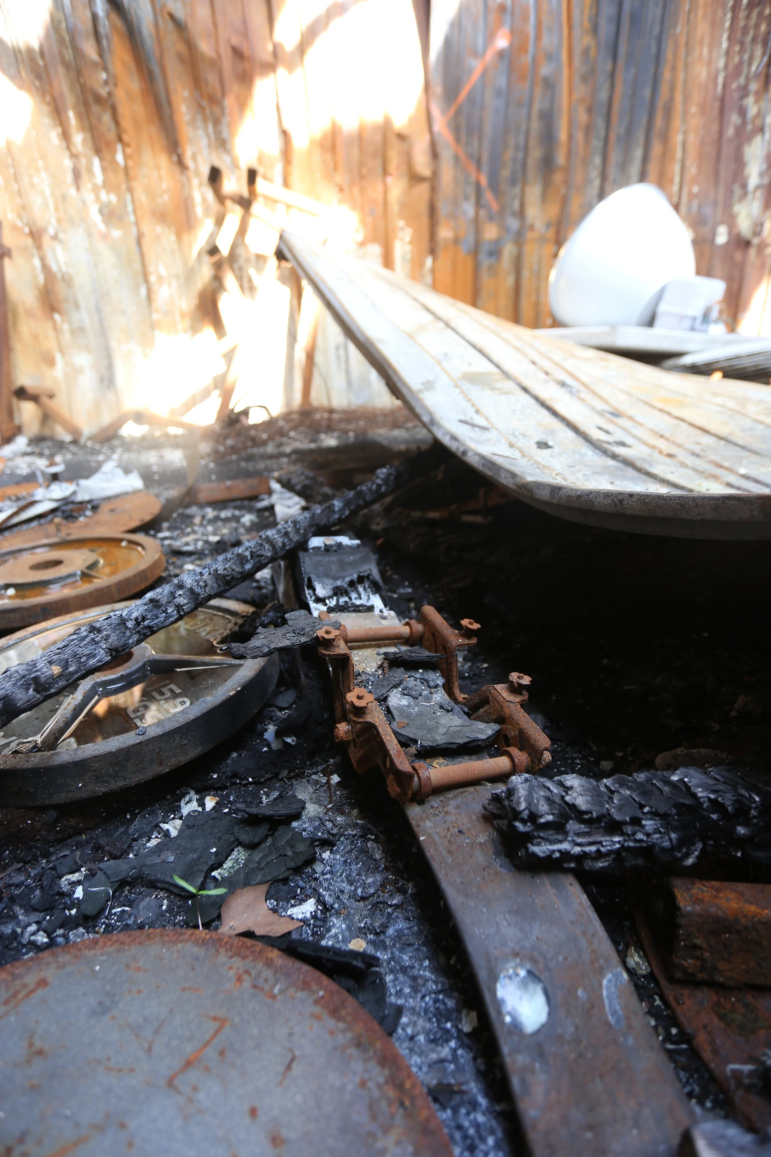 Burnt debris and burnt railroad tracks inside a burned building with wooden walls.