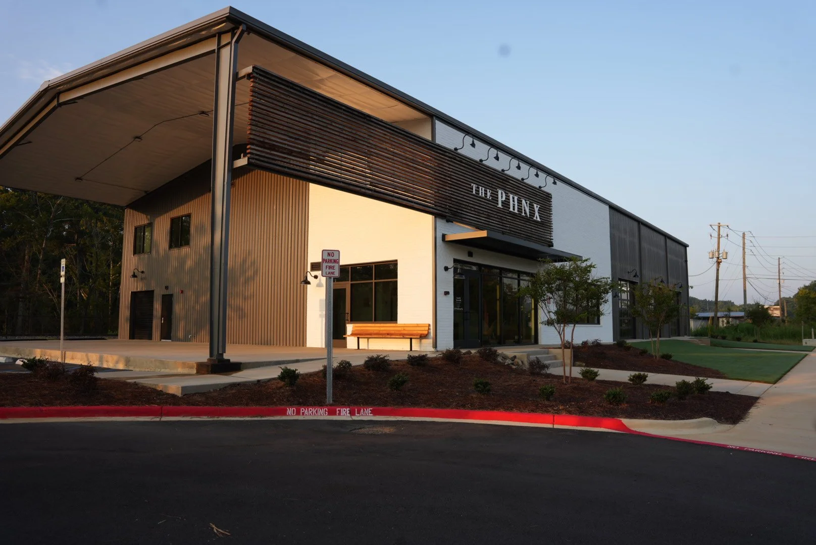Modern commercial building with a sign that reads 'The Phoenx', surrounded by a landscaped area, parking signage, and power lines in the background.