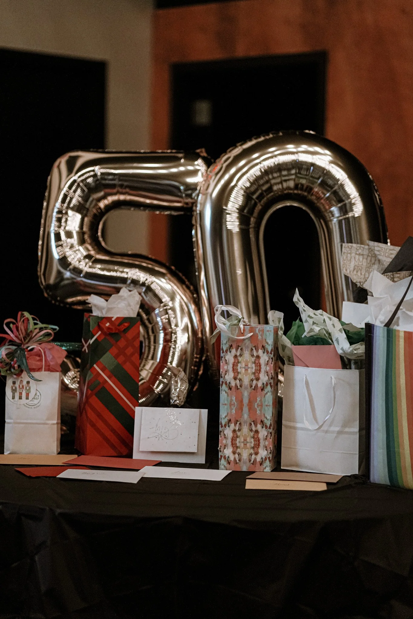 Silver '50' balloons surrounded by wrapped gifts and cards on a black table.