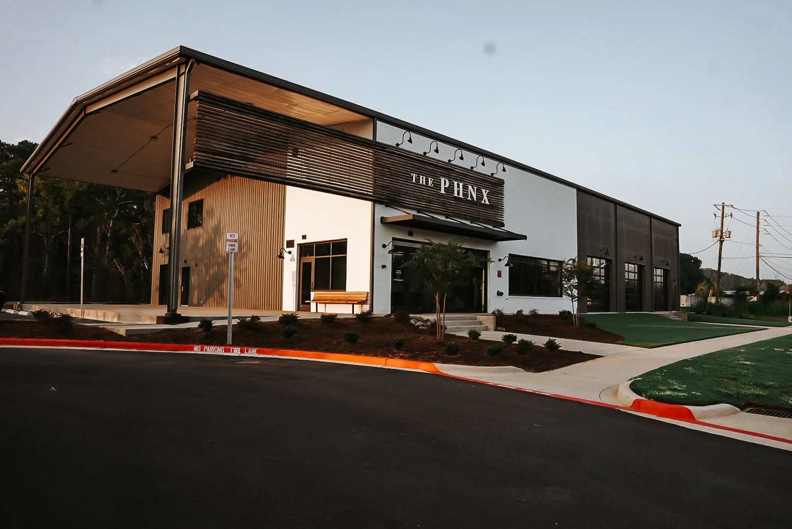 Modern commercial building named THE PHNX with a black and white exterior, large windows, and a landscaped front yard, situated along a paved street with a no parking fire lane.