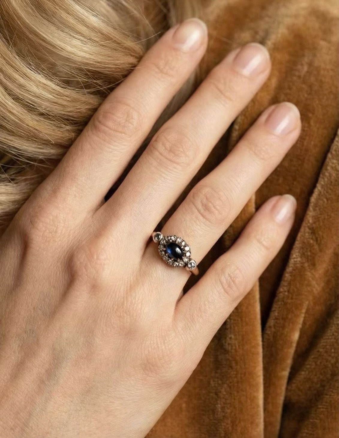 Der Cabochonschliff bei diesem Ring betont weniger Brillanz als vielmehr die Farbtiefe und innere Struktur des Saphirs, dessen dunkler, changierender Blauton je nach Lichteinfall unterschiedliche Nuancen zeigt. Umgeben wird der Saphir von einem Kranz