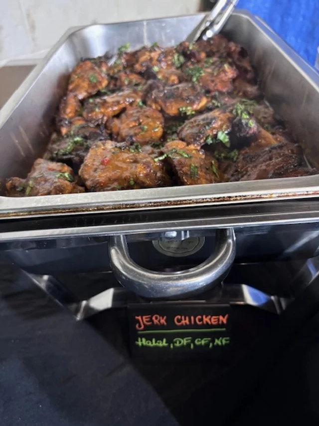 Chafing dish filled with cooked jerk chicken garnished with herbs