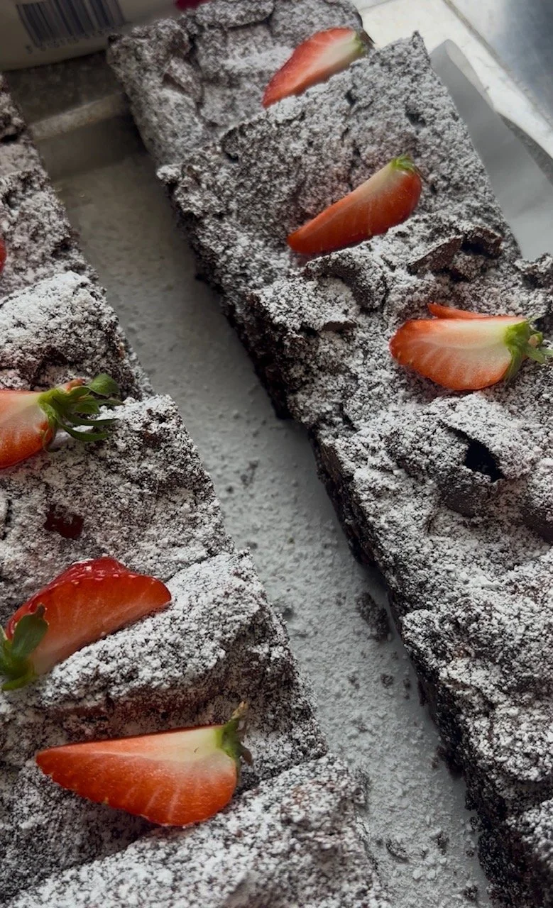 Chocolate brownies topped with powdered sugar and sliced strawberries.
