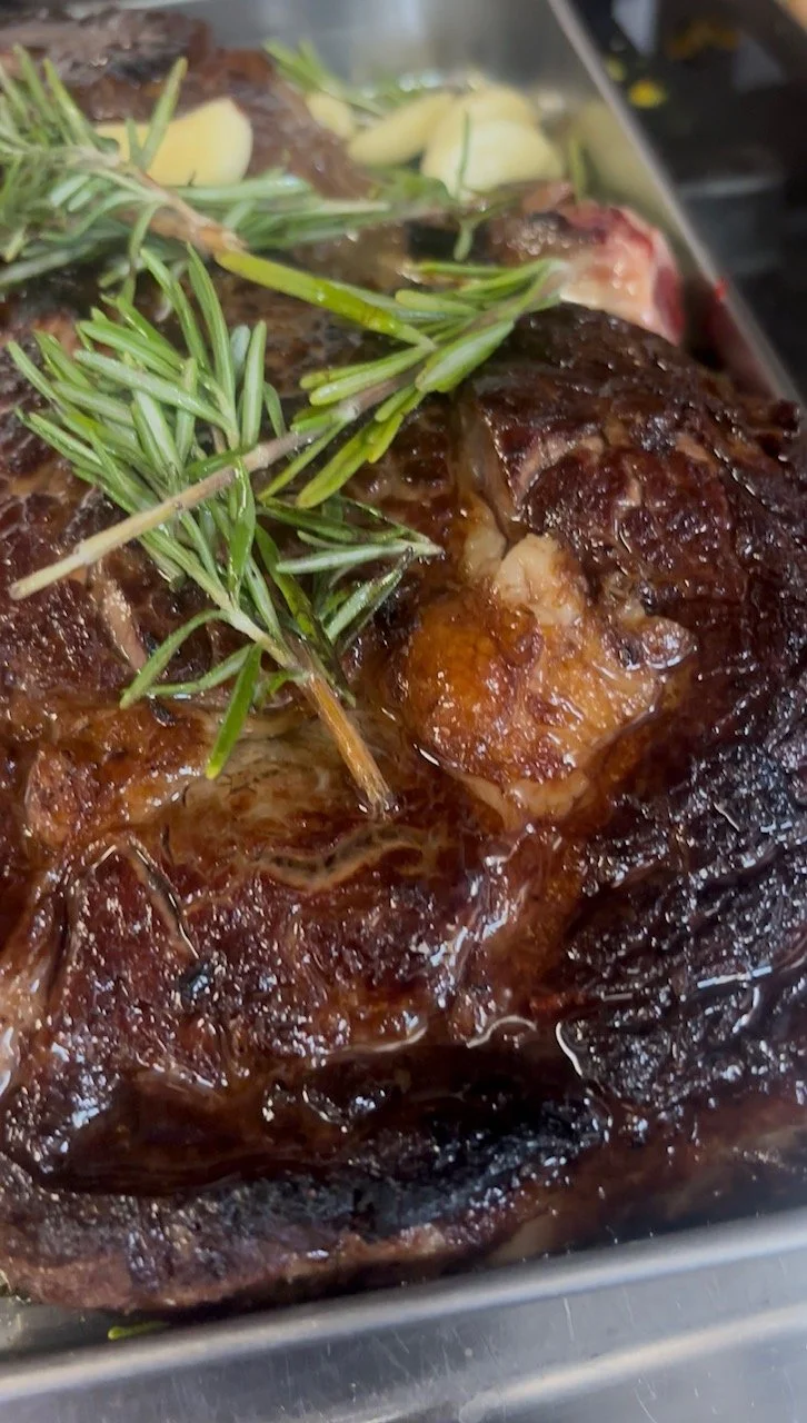 Close-up of a cooked roasted beef roast garnished with fresh rosemary sprigs and topped with slices of garlic.