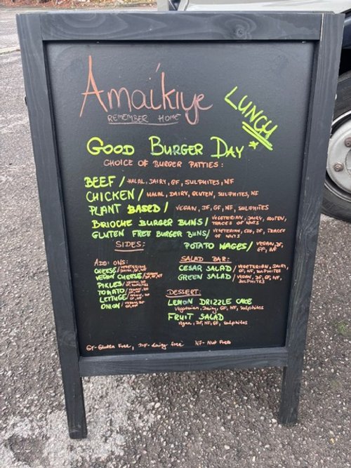 Restaurant deli-style menu chalkboard sign with offerings for burger day, including beef, chicken, plant-based options, sides like potato wedges and salads, and desserts.