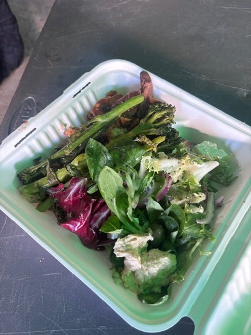 Mixed fresh salad with various greens like spinach and lettuce in a takeout container.