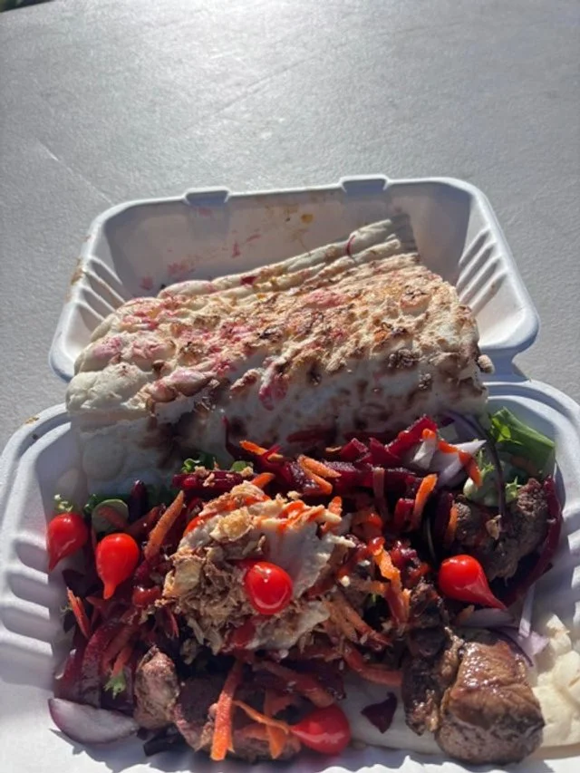 A styrofoam takeout container with a breaded fish fillet and a side salad containing cherry tomatoes, shredded carrots, and greens.