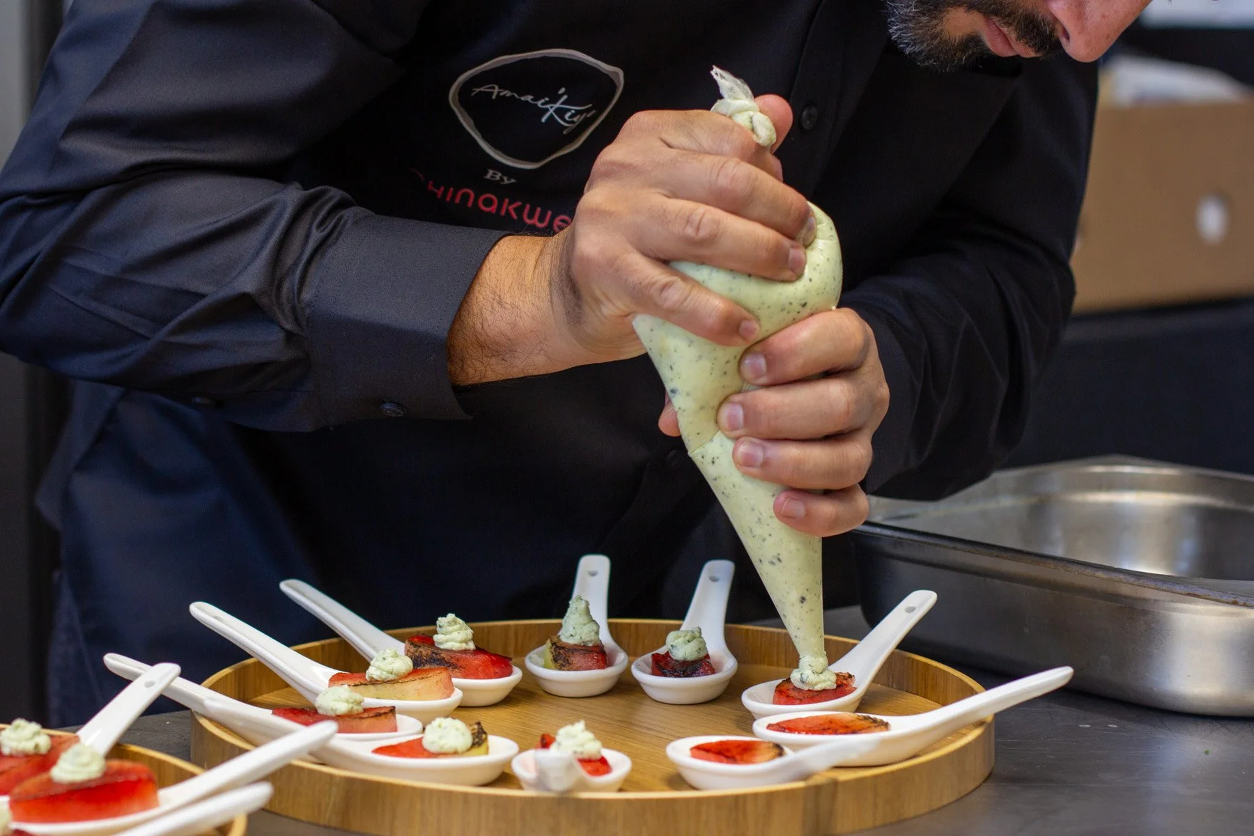 A chef is piping a creamy mixture onto plated desserts in white spoons on a wooden tray.