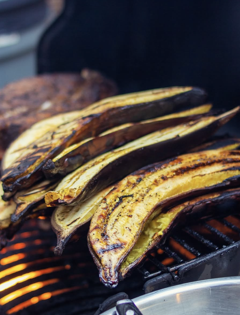 Grilled eggplants and a grilled piece of meat cooking on a barbecue grill.