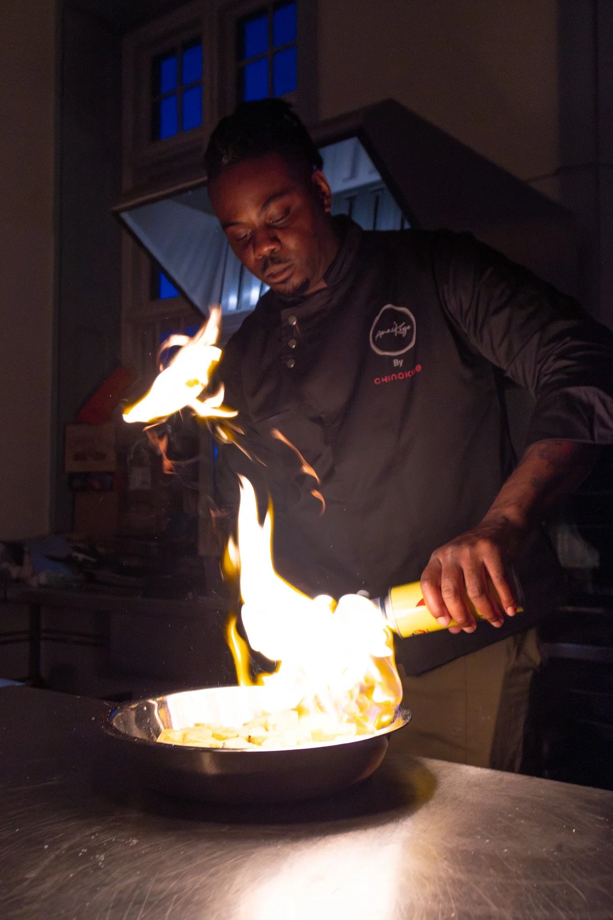 Chef igniting a flame in a frying pan in a kitchen.