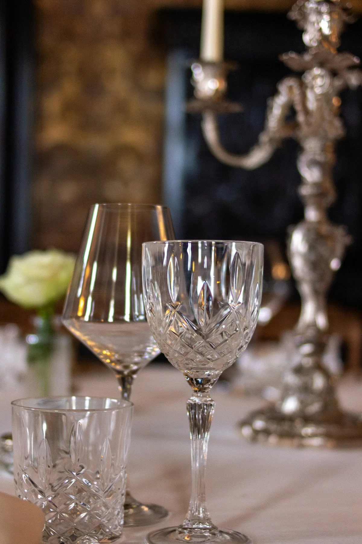 Close-up of three crystal wine glasses on a table with a blurred background of a candelabra and a brick wall.