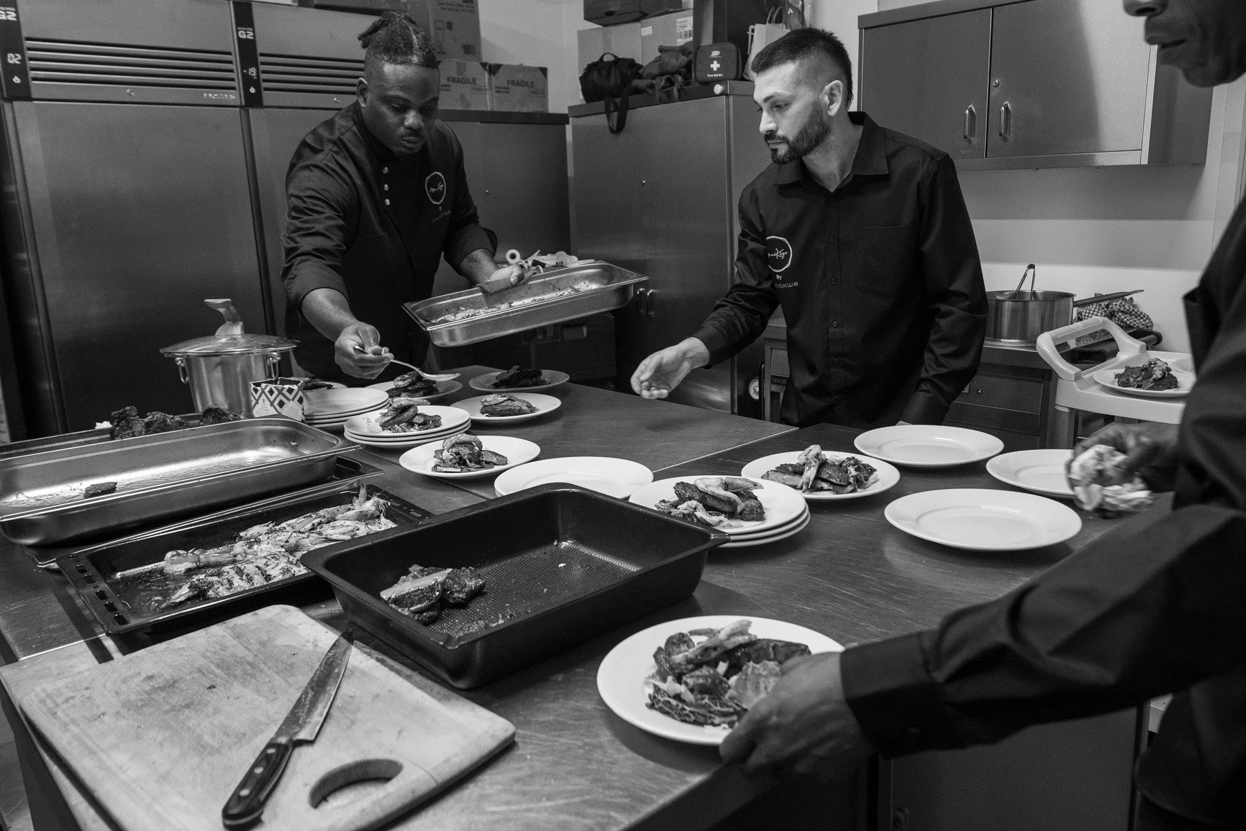 Three men preparing plates of food in a commercial kitchen.