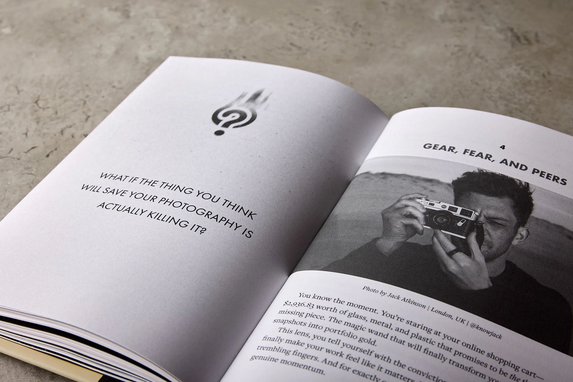 Open magazine laying on a textured surface, showing two pages. The left page has a question about photography and what might save it. The right page has a black-and-white photo of a man with curly hair holding a camera, with a caption indicating it was taken by Jack Atkinson in London, UK.