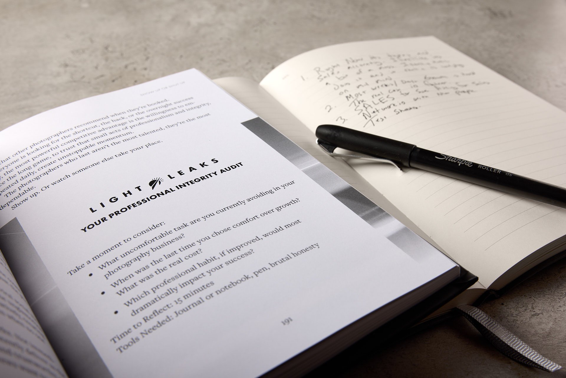 Open book with a professional integrity audit headline and questions, a pen resting on an open notebook with handwritten notes, on a desk.