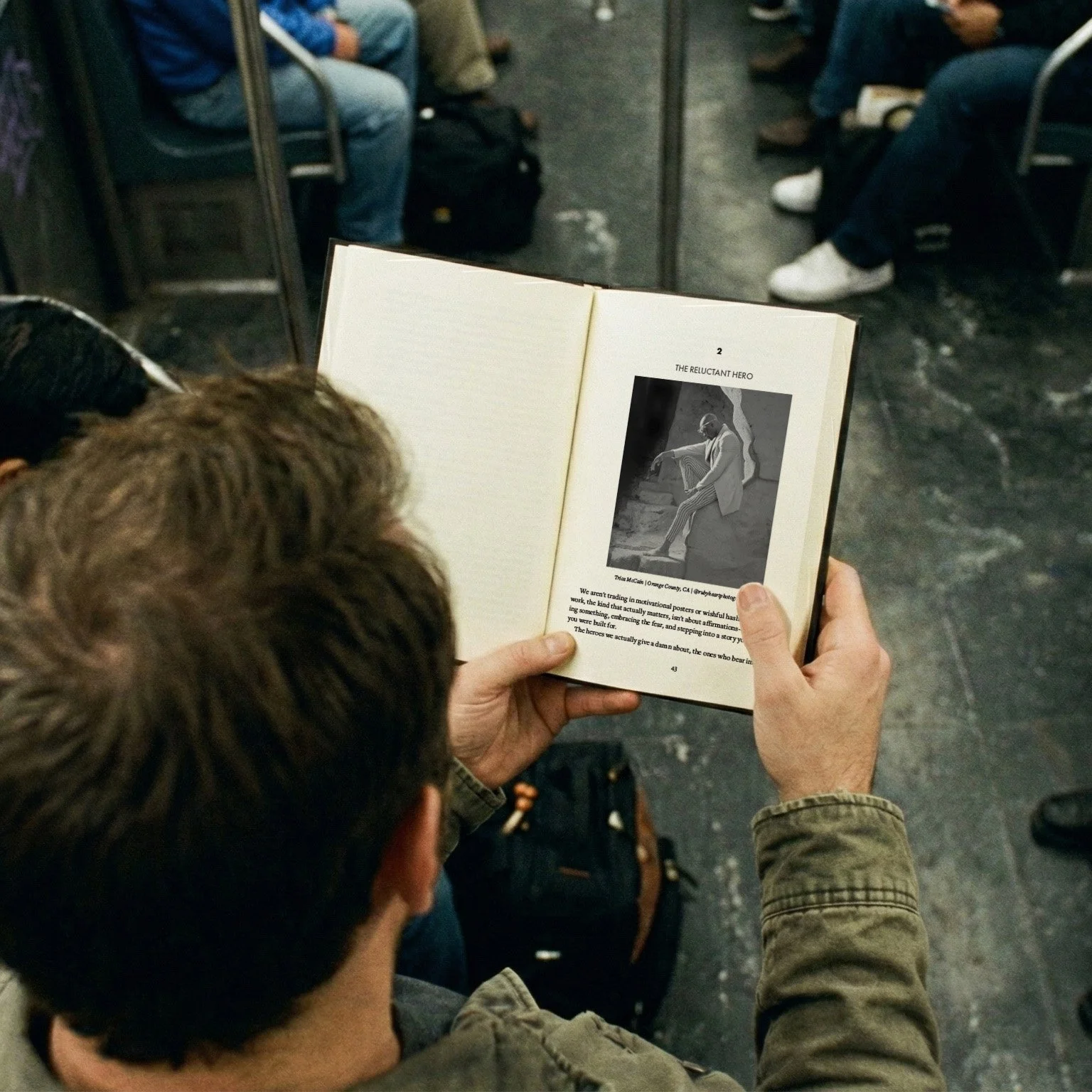 A person sitting in a subway car is reading a book that has a black-and-white photo of a person sitting on steps on its open page.