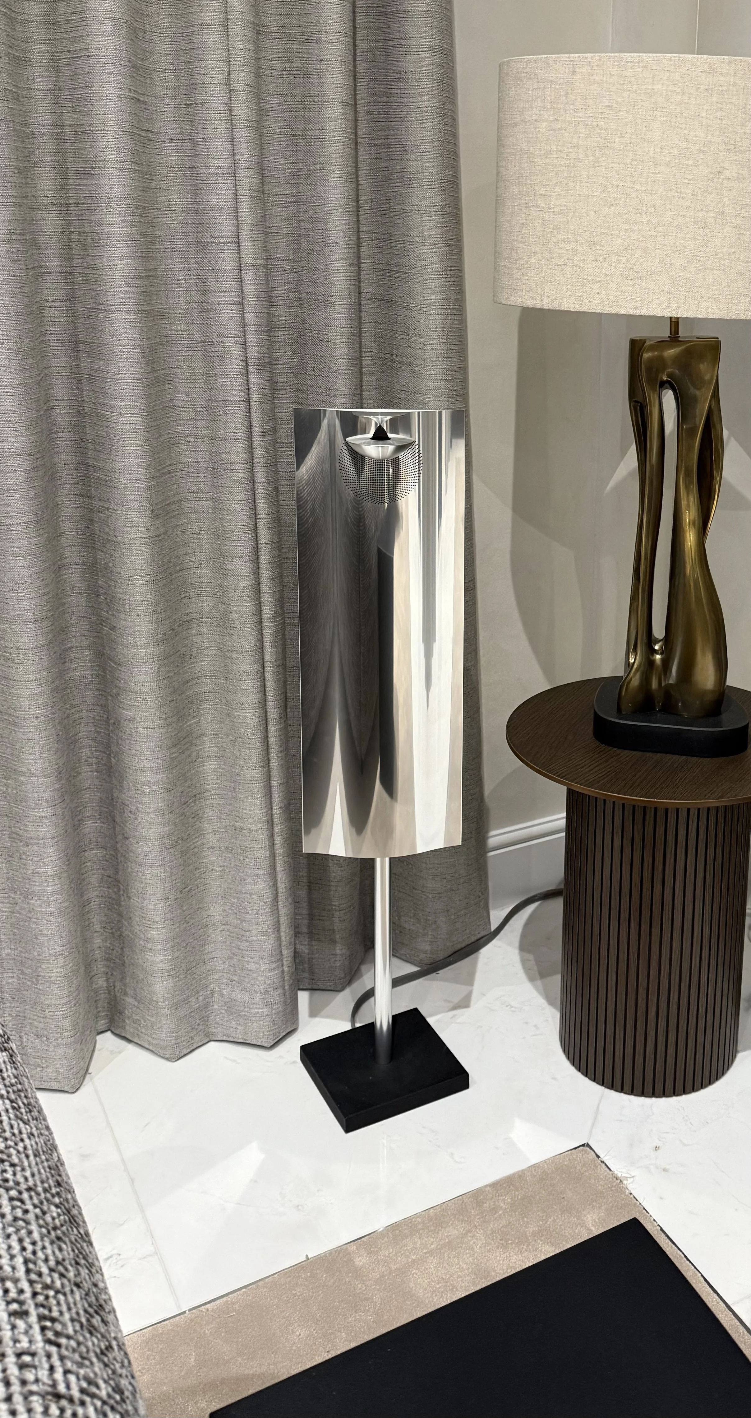 Bang & Olufsen BeoLab 12.3 floor-standing speaker in polished aluminium on a black base, displayed in a modern living room setting as a premium pre-owned, refurbished and re-loved B&O speaker.