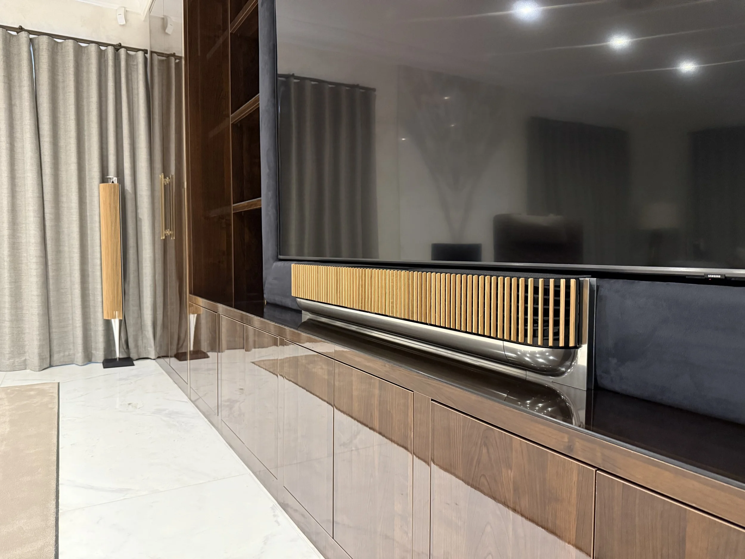Bang & Olufsen Beosound Theatre soundbar with oak lamella cover and BeoLab 18 speaker in a modern living room, displayed as premium pre-owned, refurbished and re-loved B&O audio equipment.