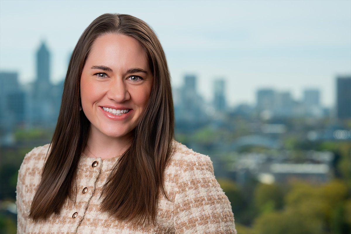 A smiling woman with long brown hair in front of a city skyline.