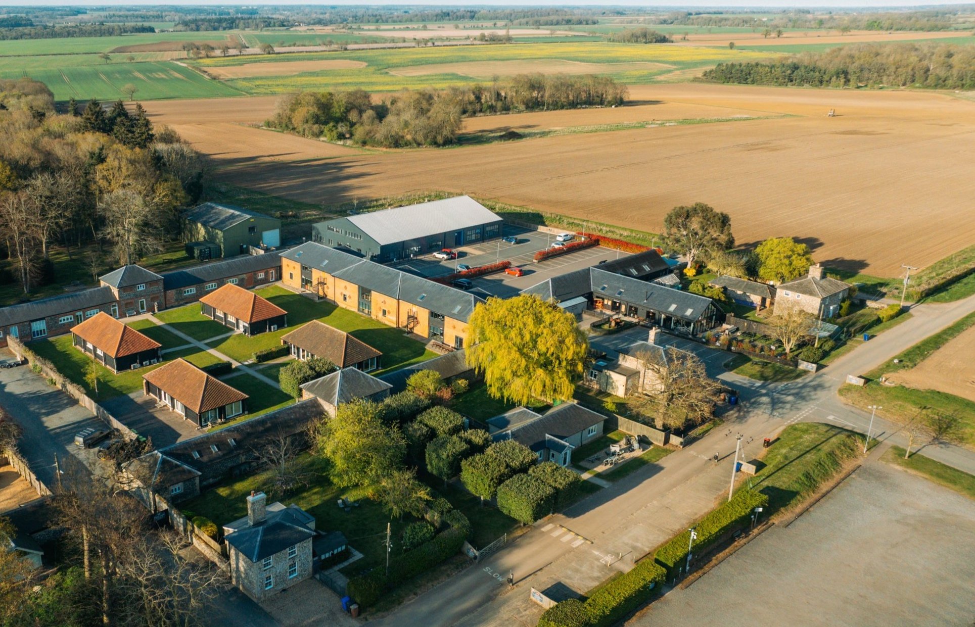Aerial view of a rural village with brick buildings, roads, greenery, and surrounding fields.