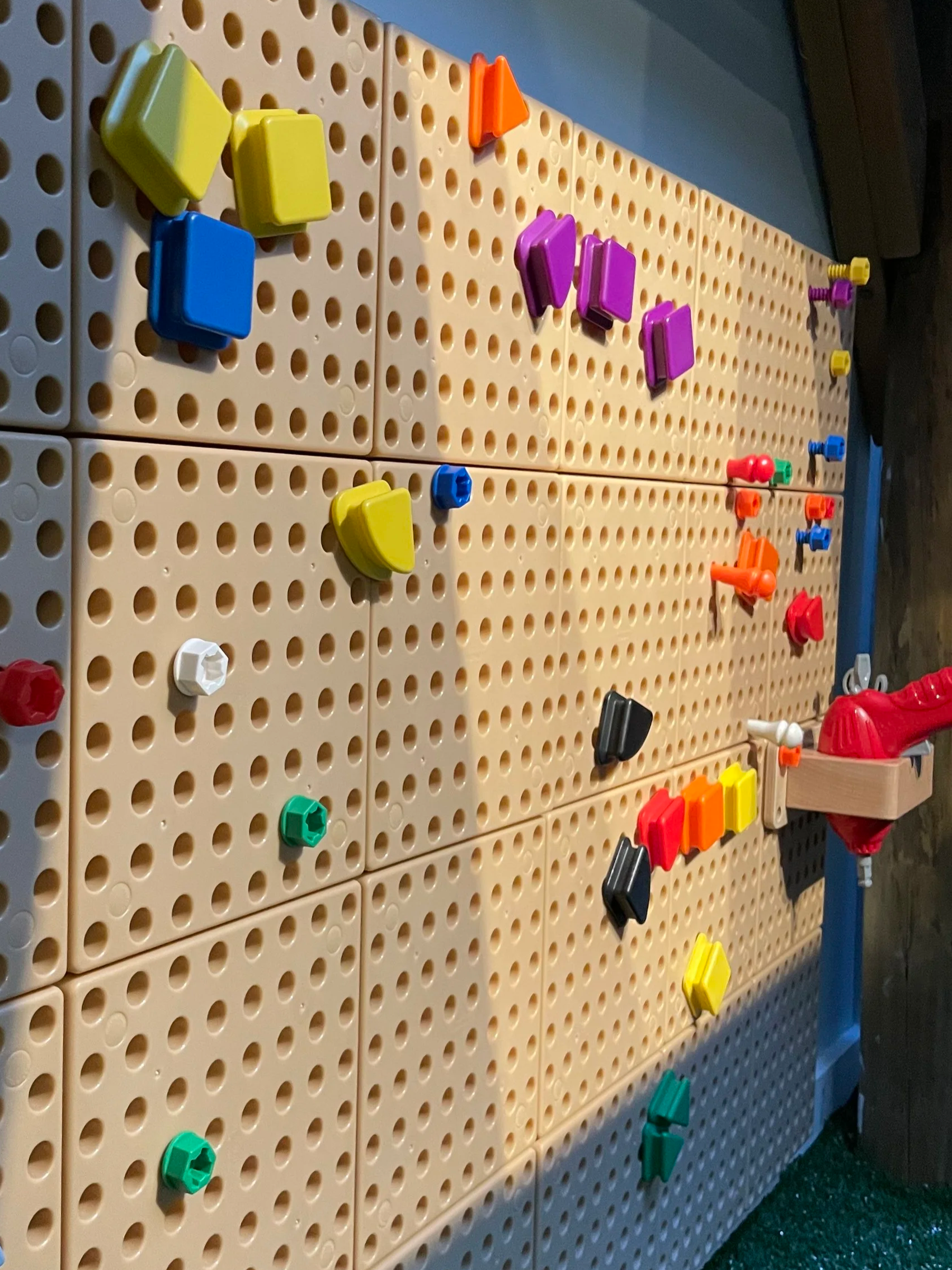 Colorful toy pegs and blocks attached to a beige pegboard for children's building play.
