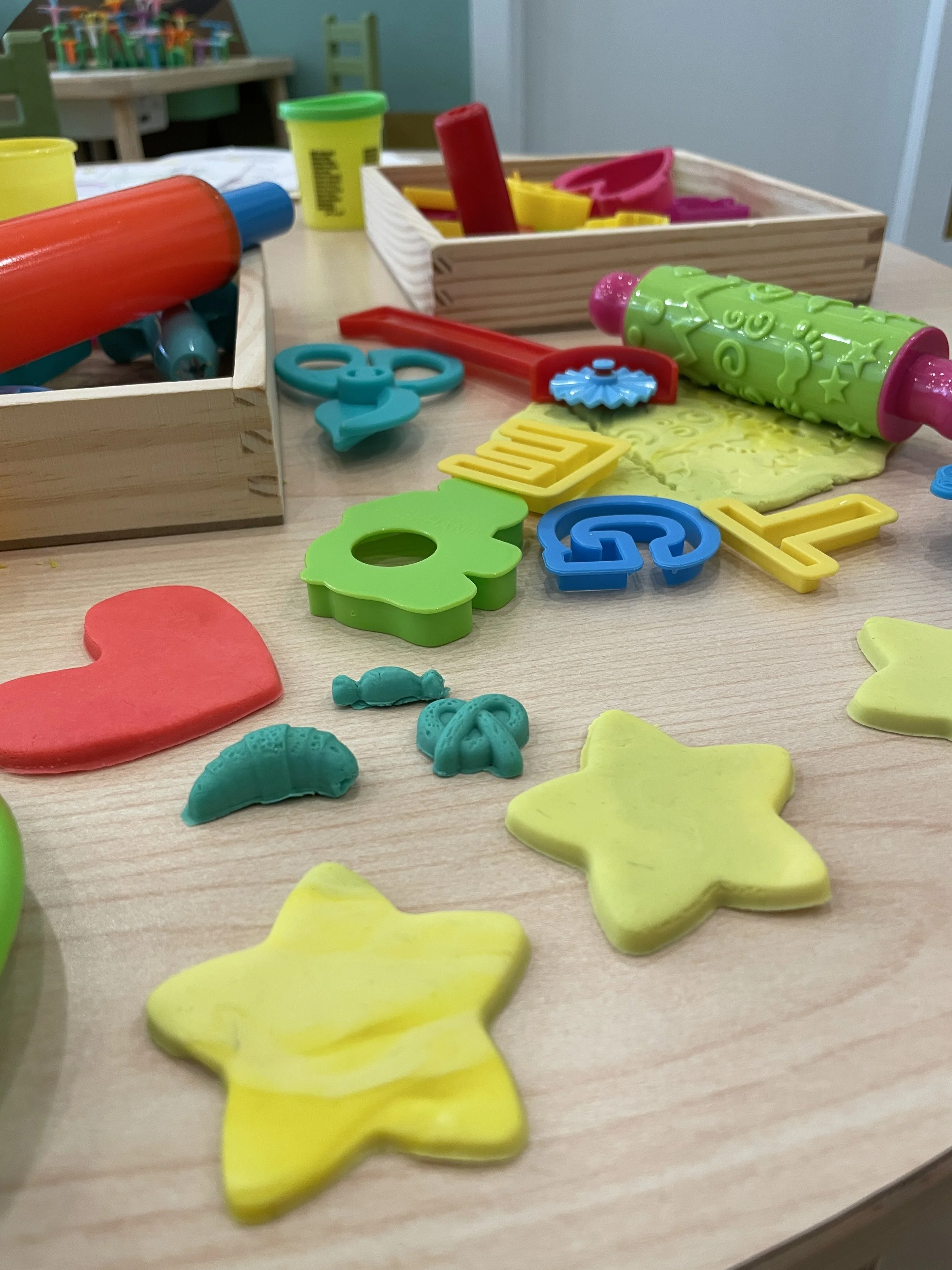 Colorful plastic toys including cookie cutters, a rolling pin, and other play dough tools on a wooden table.
