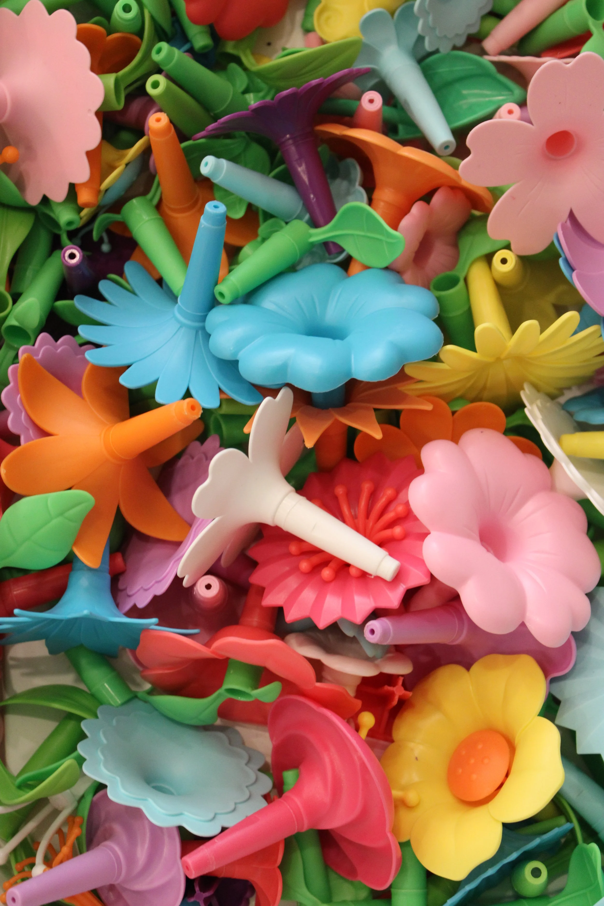 A pile of colorful plastic flower and leaf-shaped novelty straws and straw accessories.