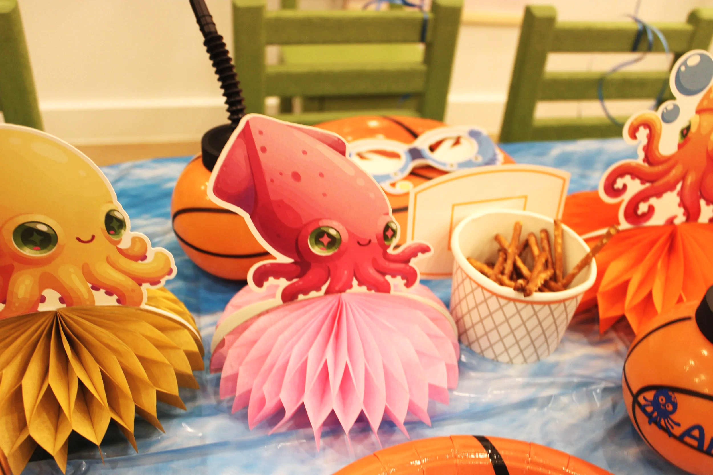 Colorful decorations with cartoon-style sea creatures such as an octopus and an octopus, along with paper lanterns and a small bucket, on a blue tablecloth, likely for a party or celebration.