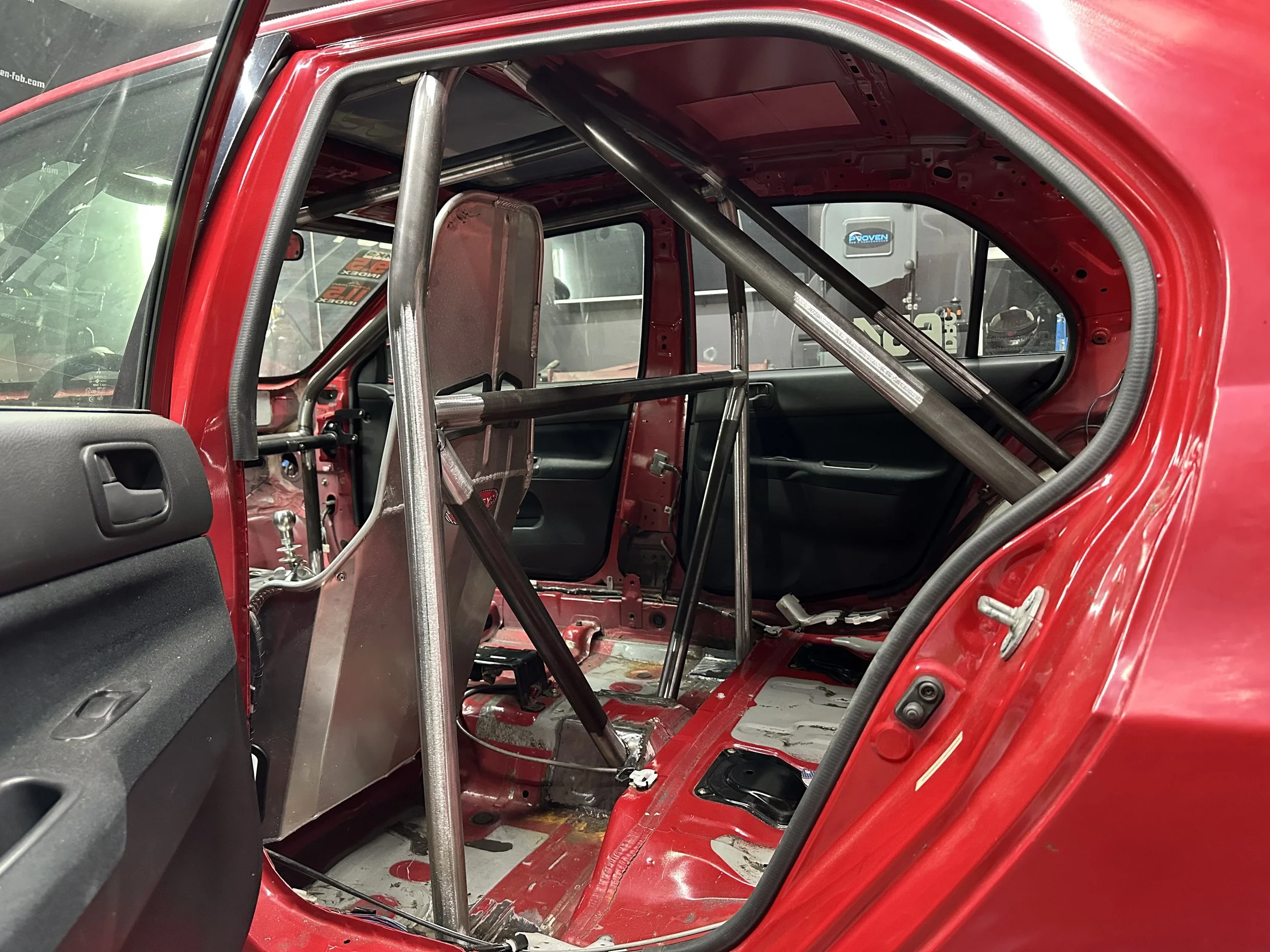 Inside of a red race car with a metal roll cage and no seats.