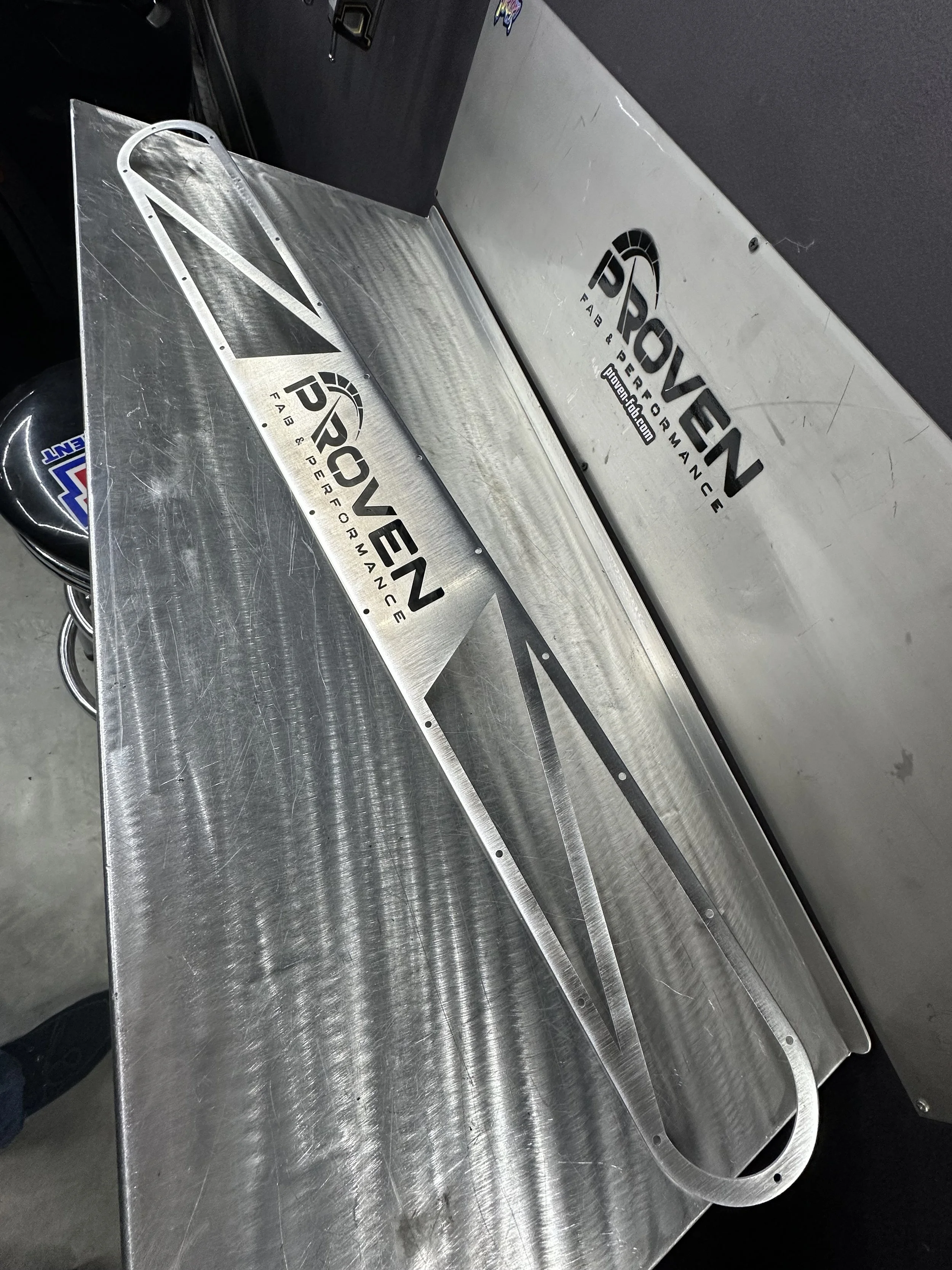 A metal airplane wing with the PR0VEN logo and website, placed on a table with a black backdrop.
