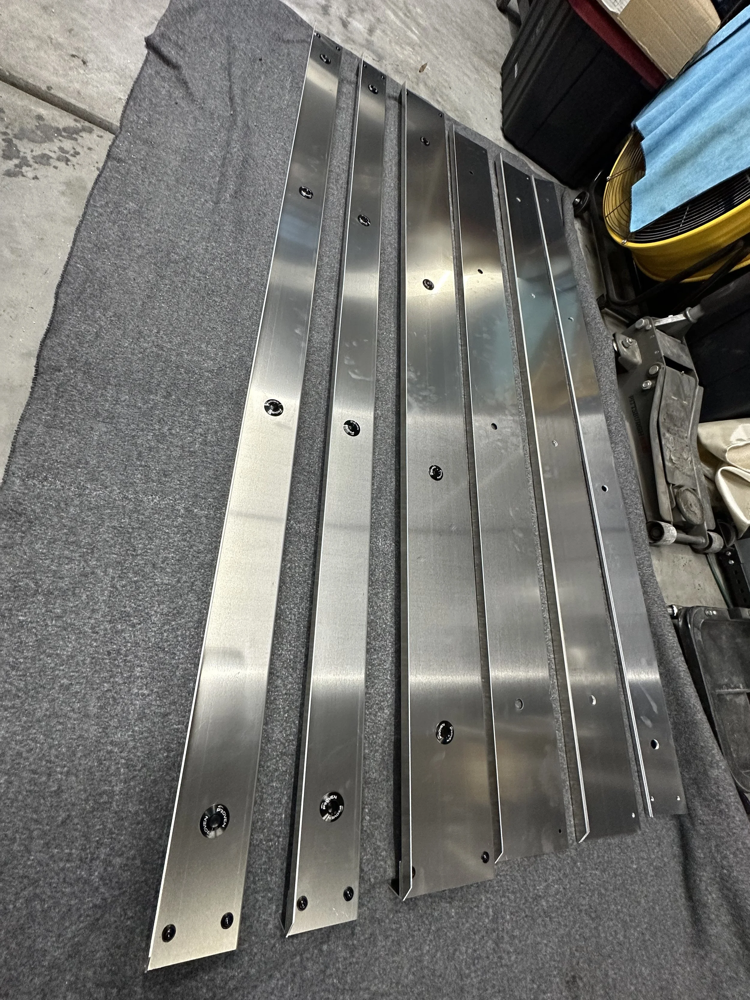 Four metallic elongated parts with screw holes placed on a flat surface.