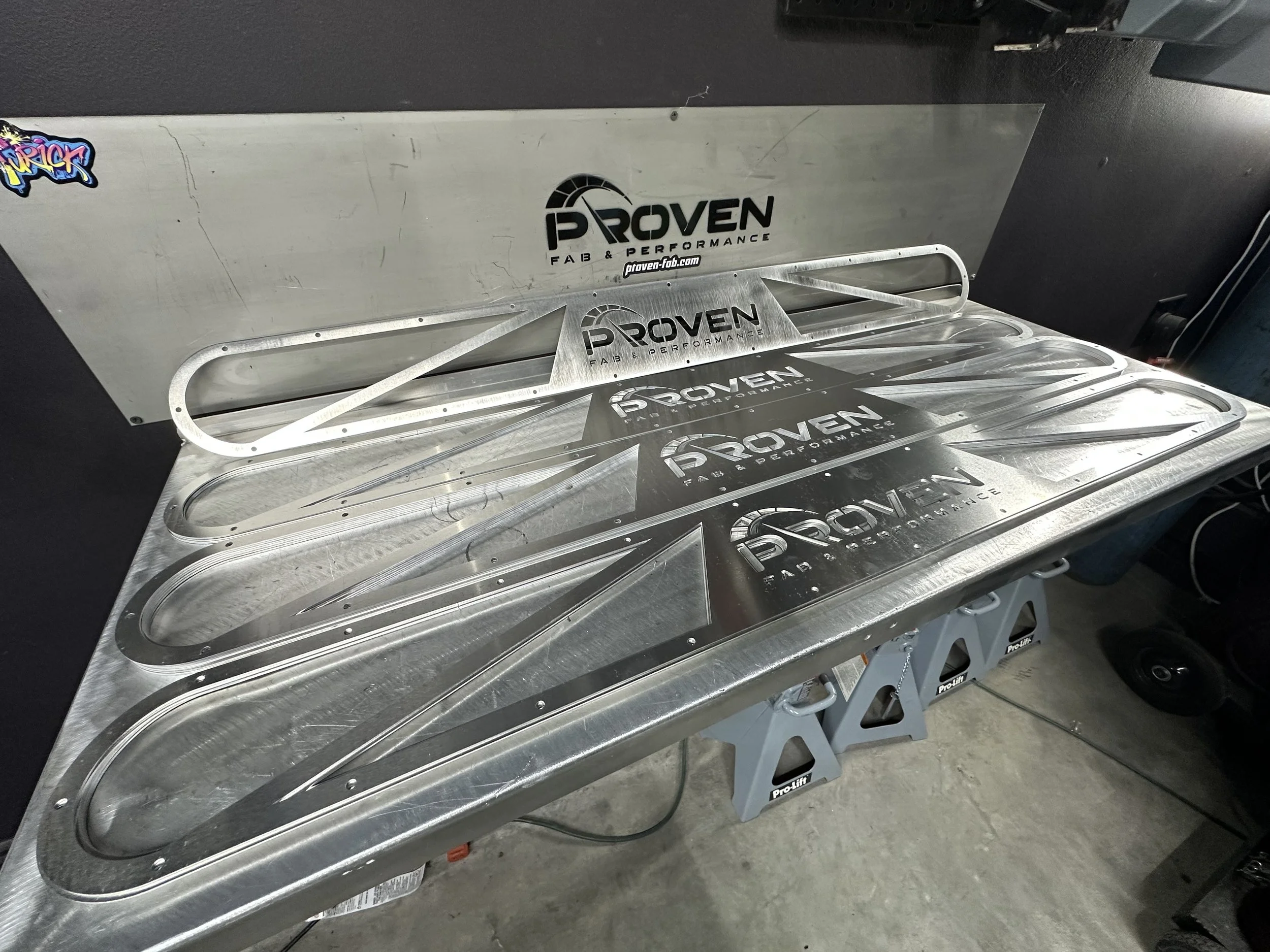 Metalized aluminum racing car radiator support with Proven Performance logo, placed on foldable stand.