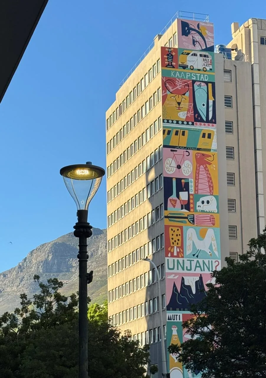 Colorful mural on a multi-story building in Cape Town, featuring abstract and stylized animals, landmarks, and text.