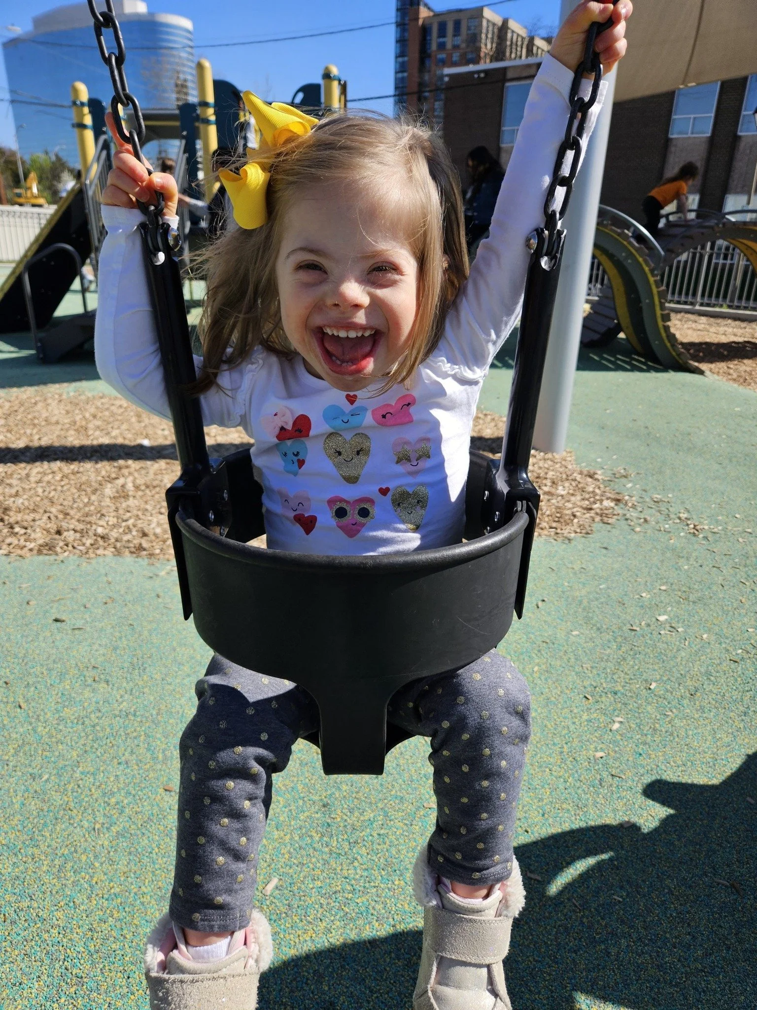 A Caucasian toddler with Down syndrome sitting in a swing smiling
