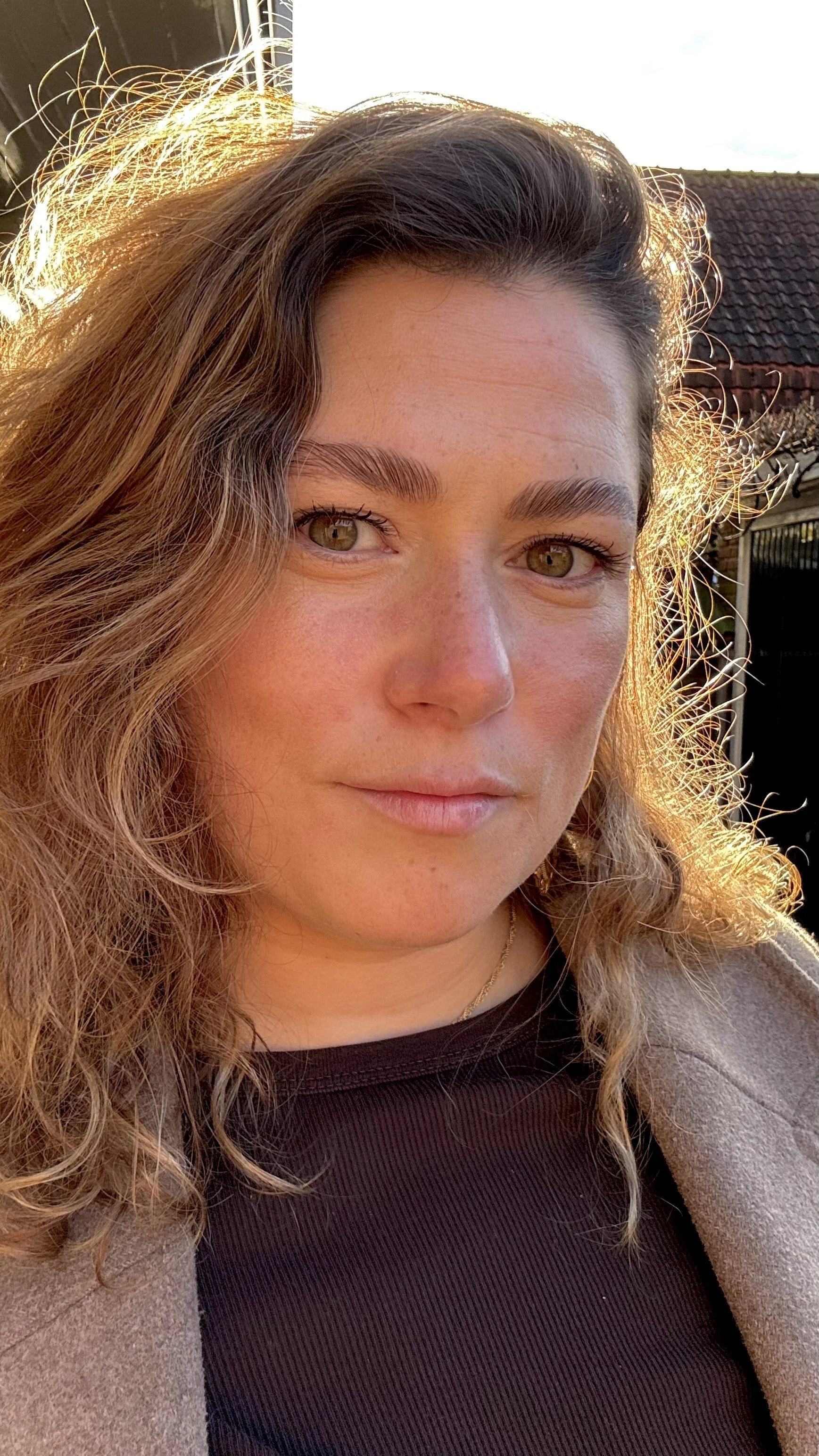 Close-up van een vrouw met lichtbruine, golvende haar en lichte huid, in de buitenlucht bij zonsondergang.