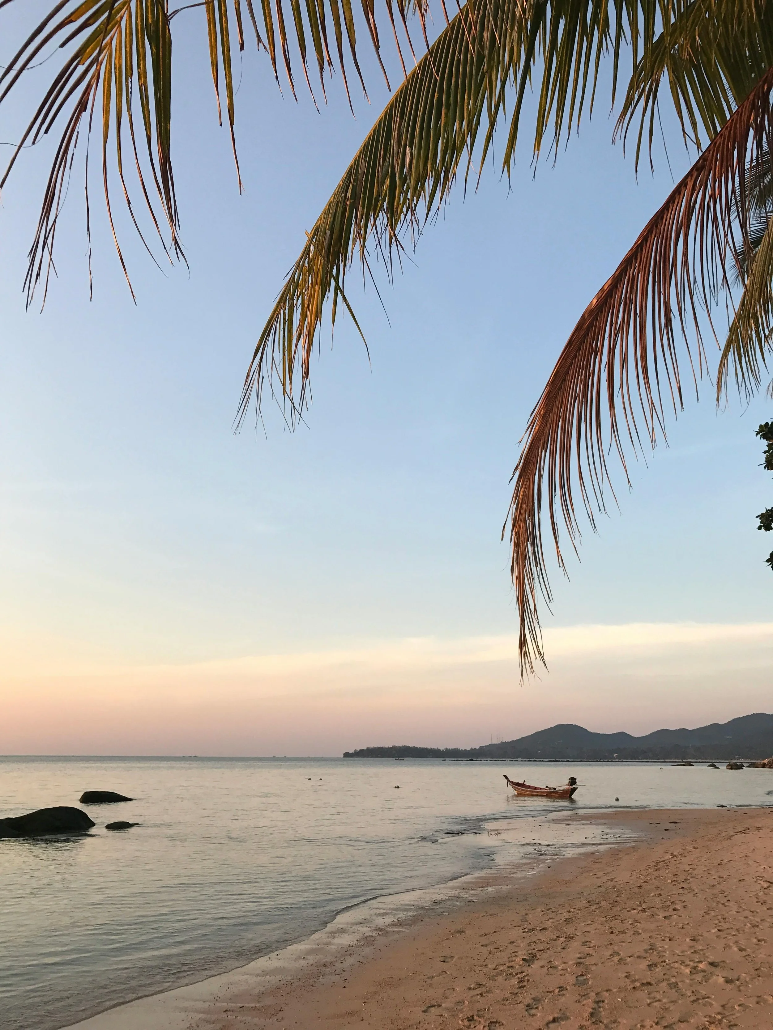 Calm beach at sunset with a longtail boat on still water, representing the life-work balance freelance designers want back when their business runs with structure