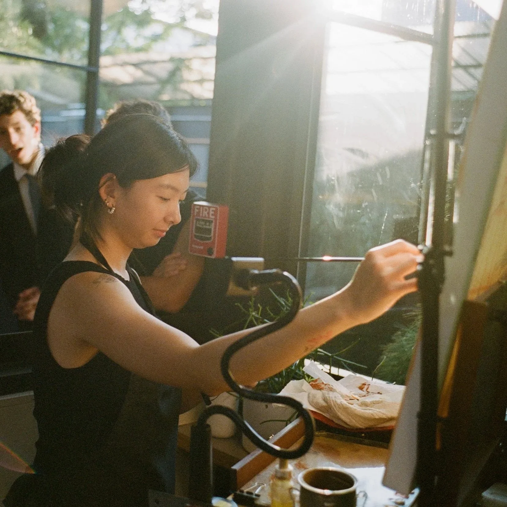 A woman preparing food behind a counter, with sunlight shining through a window behind her.