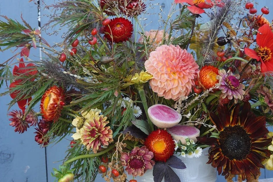 A colorful bouquet of mixed flowers including dahlias, sunflowers, and berries, arranged in a vase.