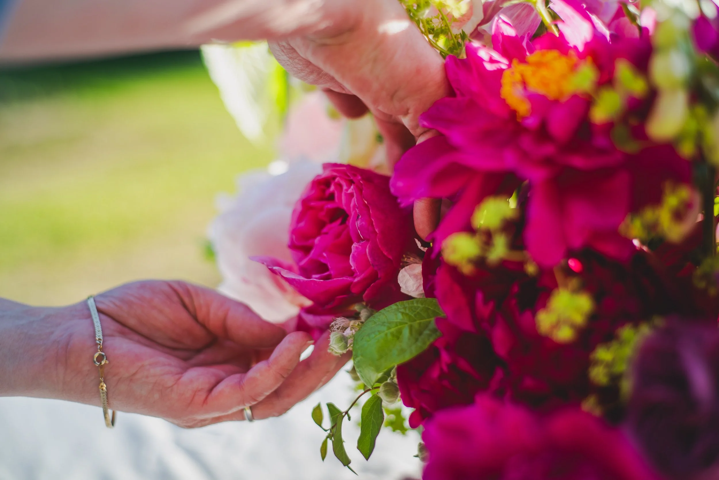 A close-up of a person's hands arranging colorful pink and purple flowers outdoors.