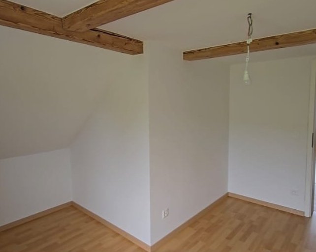 Empty room with white walls, wooden floor, and exposed wooden beams on the ceiling.